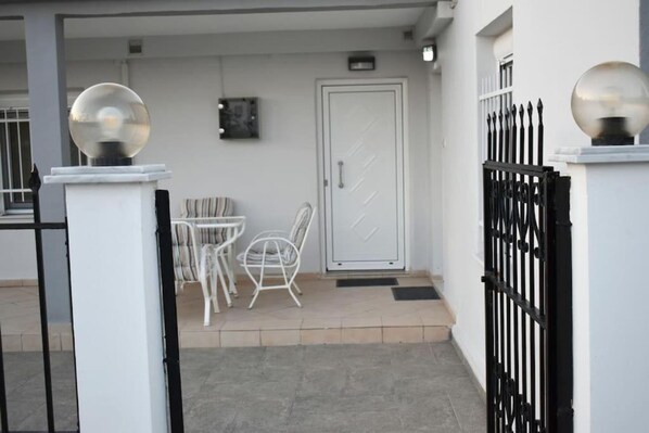 A gated entrance with a white door, a small outdoor seating area with chairs, and a spherical light fixture on a pedestal. - Avli Guesthouse (Trikala)
