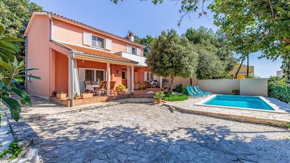 A two-story house with a covered patio, a swimming pool, and a garden.