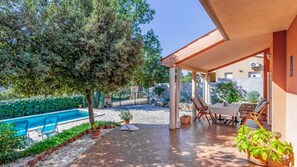 A covered outdoor area with a pool, lounge chairs, and potted plants.