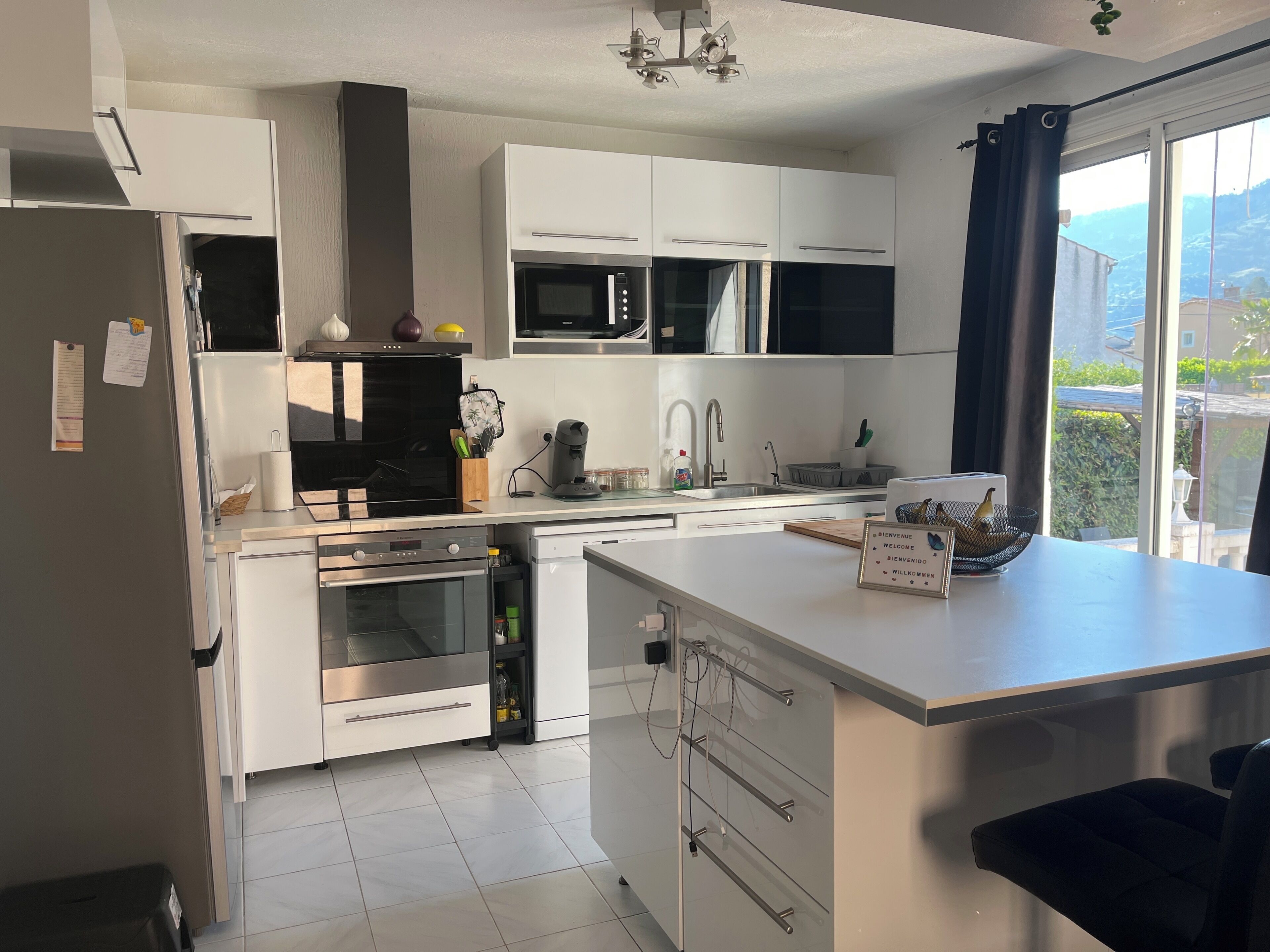 A modern kitchen with white cabinets, a built-in oven, microwave, and a large island with a sink.