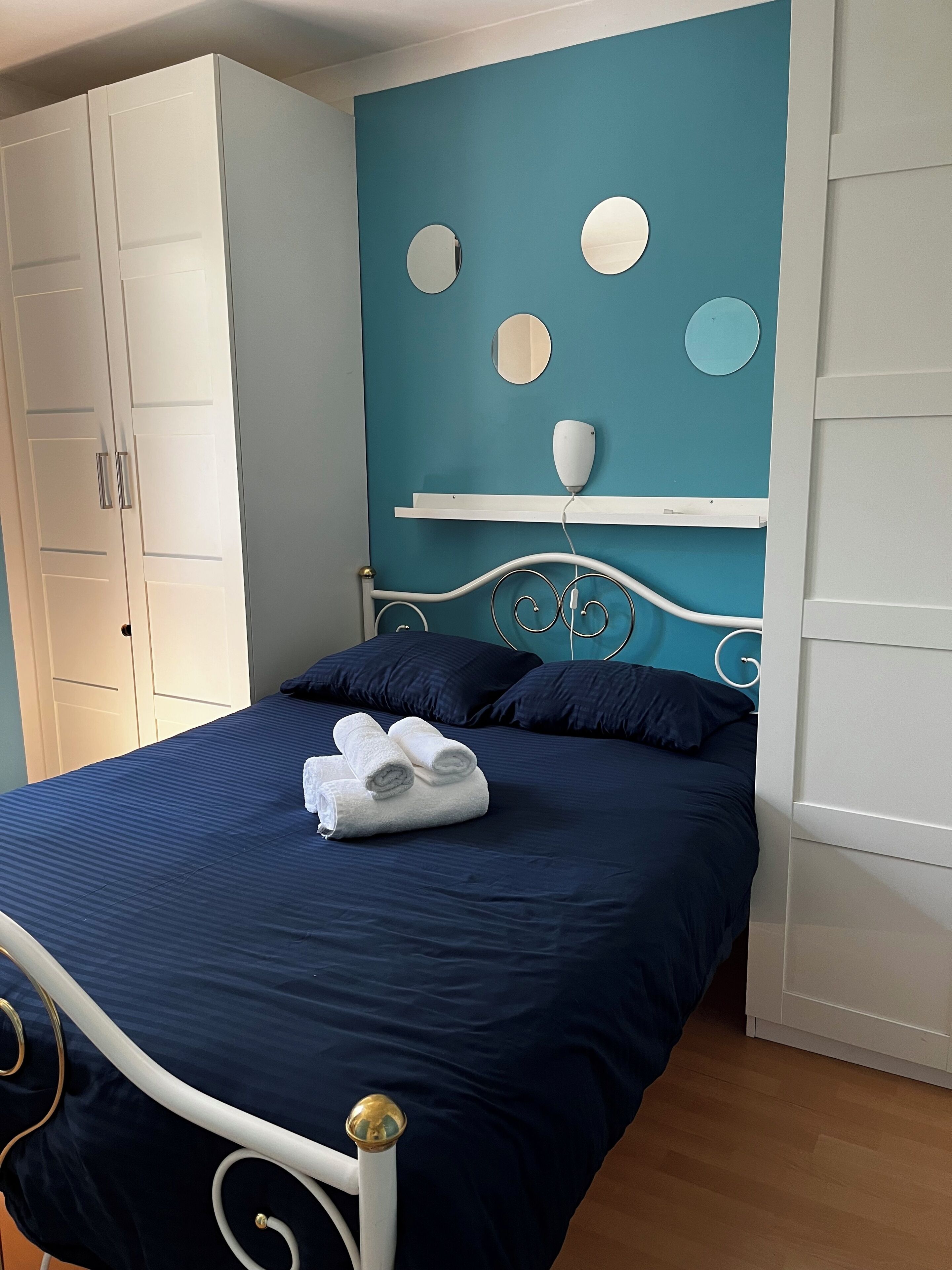 A bed with a white metal frame, a teal wall with circular mirrors, and a white wardrobe.