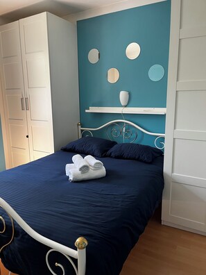 Un lit avec une couvre-lit bleue, une tête de lit blanche et une armoire blanche avec un miroir.