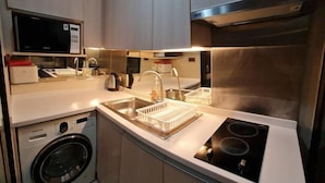 Een compacte keuken met een ingebouwde wasmachine en droger, roestvrijstalen apparatuur en een magnetron op een plank.