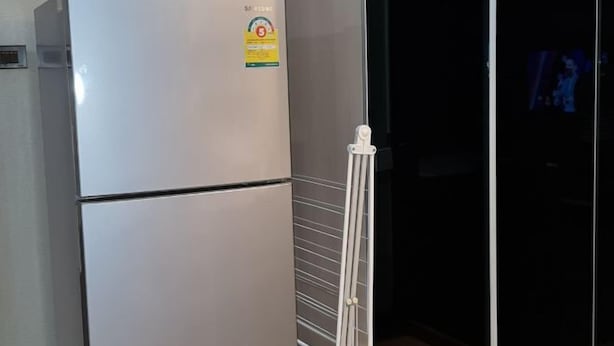 Un réfrigérateur blanc orné d’un autocollant, une étagère métallique blanche et une pièce sombre avec une porte visible.