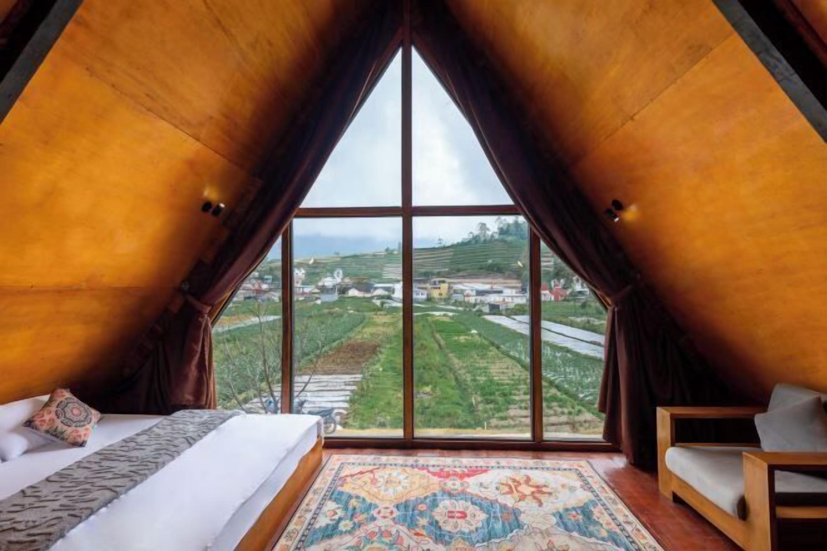 A room with a large window, a bed, a sofa, and a patterned rug.