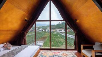 A room with a large window, a bed, a sofa, and a patterned rug.