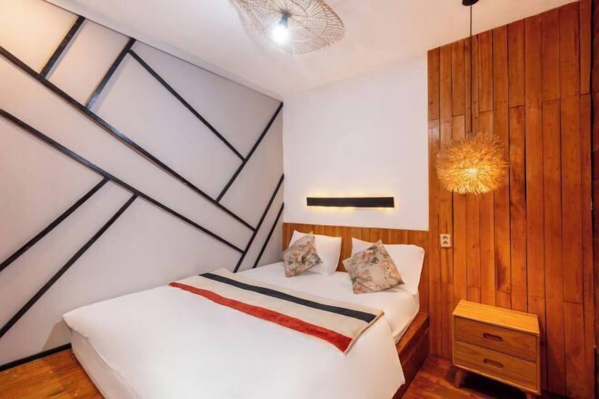 A modern bedroom with a bed, bedside table, and a unique ceiling light fixture.