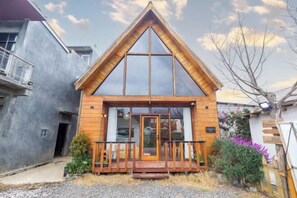 Una cabaña de madera con techo triangular, ventanas grandes y un porche de madera.