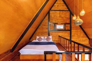 Un dormitorio acogedor en el ático, con techo inclinado de madera, cama con almohadones estampados e iluminación colgante.