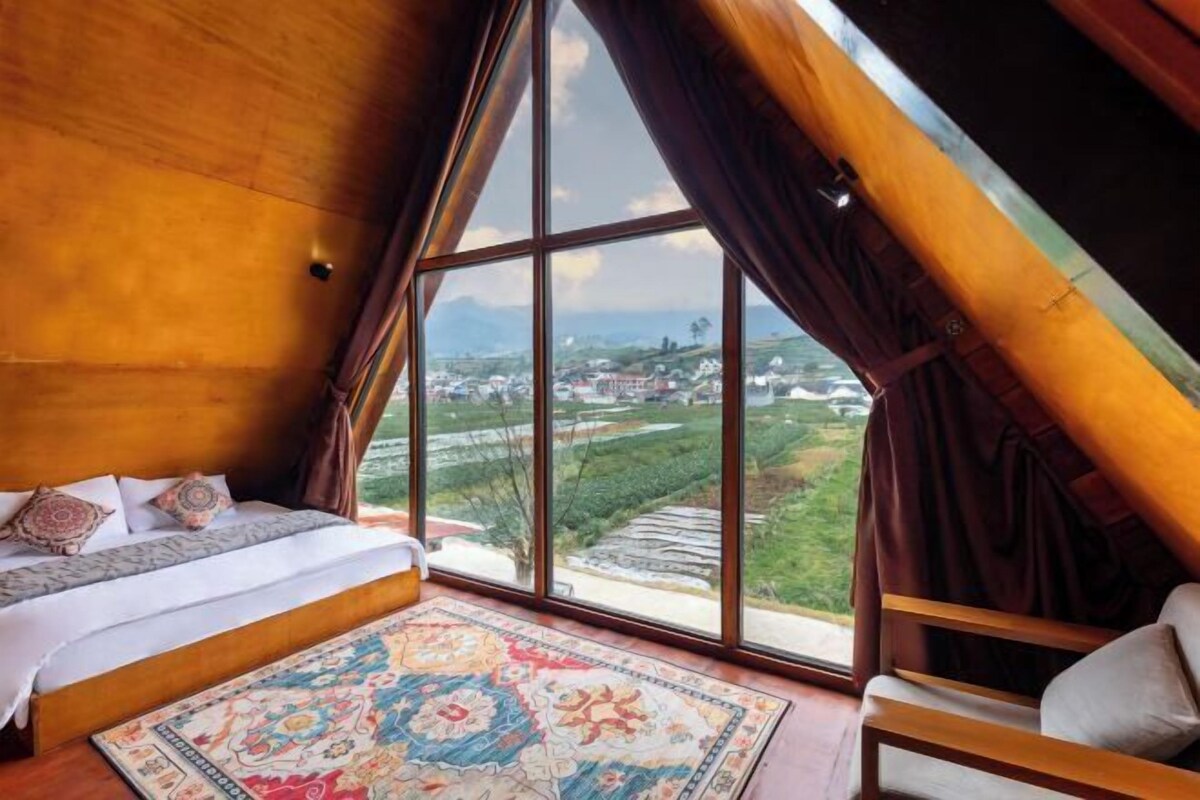 Een slaapkamer met een groot raam, een bed, een stoel en een kamerkleed met een patroon.