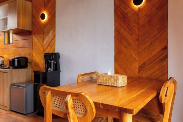 Una mesa de comedor de madera con sillas, una cafetera y una cesta con una caja de pañuelos.
