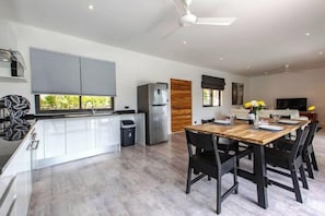 A modern kitchen with a dining area, a built-in oven, and a large window. - Villa Nirvana (Koh Samui)