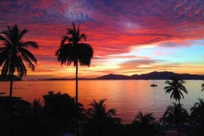 Un coucher de soleil sur une mer calme, avec des palmiers se découpant en silhouette sur le ciel.