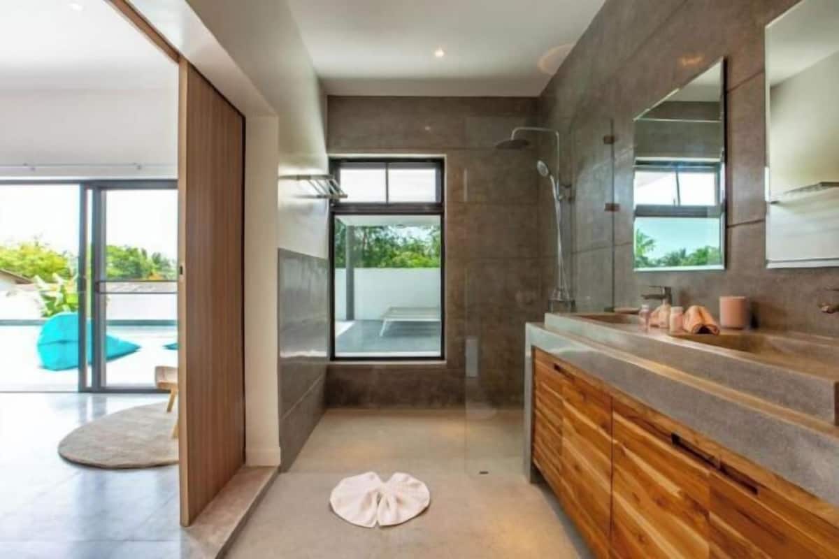A modern bathroom with a large mirror, wooden cabinets, and a shower area.