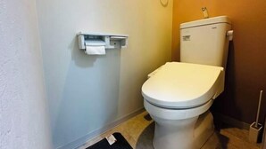 Un baño pequeño y funcional con inodoro blanco, dispensador de toallas de papel en la pared y cepillo para inodoro.