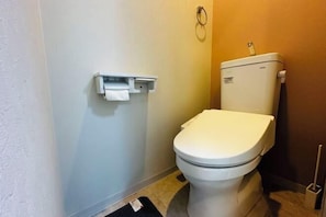 Un baño pequeño y funcional con inodoro blanco, dispensador de toallas de papel en la pared y cepillo para inodoro.