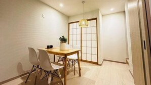 Un comedor con una mesa de madera y sillas blancas, una lámpara colgante y una puerta corredera con paneles shoji.