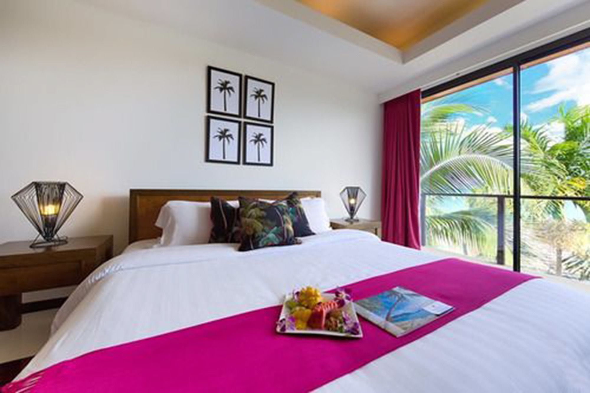 Una habitación de hotel con una cama grande, vistas a palmeras y una ventana con cortinas rojas.