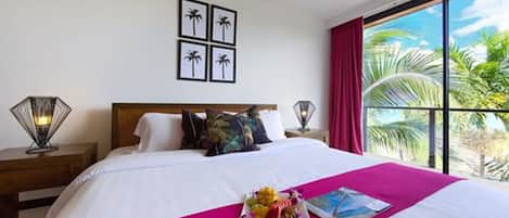 Una habitación de hotel con una cama grande, vistas a palmeras y una ventana con cortinas rojas.