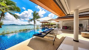 An infinity pool with lounge chairs, a covered seating area, and a view of the ocean. - Baan Benjamart (Koh Samui)
