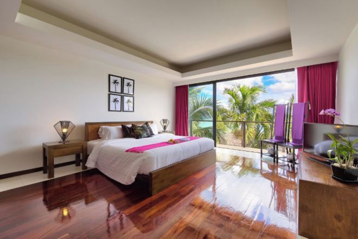 A hotel room with a large bed, a nightstand, a TV, and a view of palm trees.