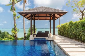 A pool with a view of the sea, a covered seating area, and lush greenery. - Baan Benjamart (Koh Samui)
