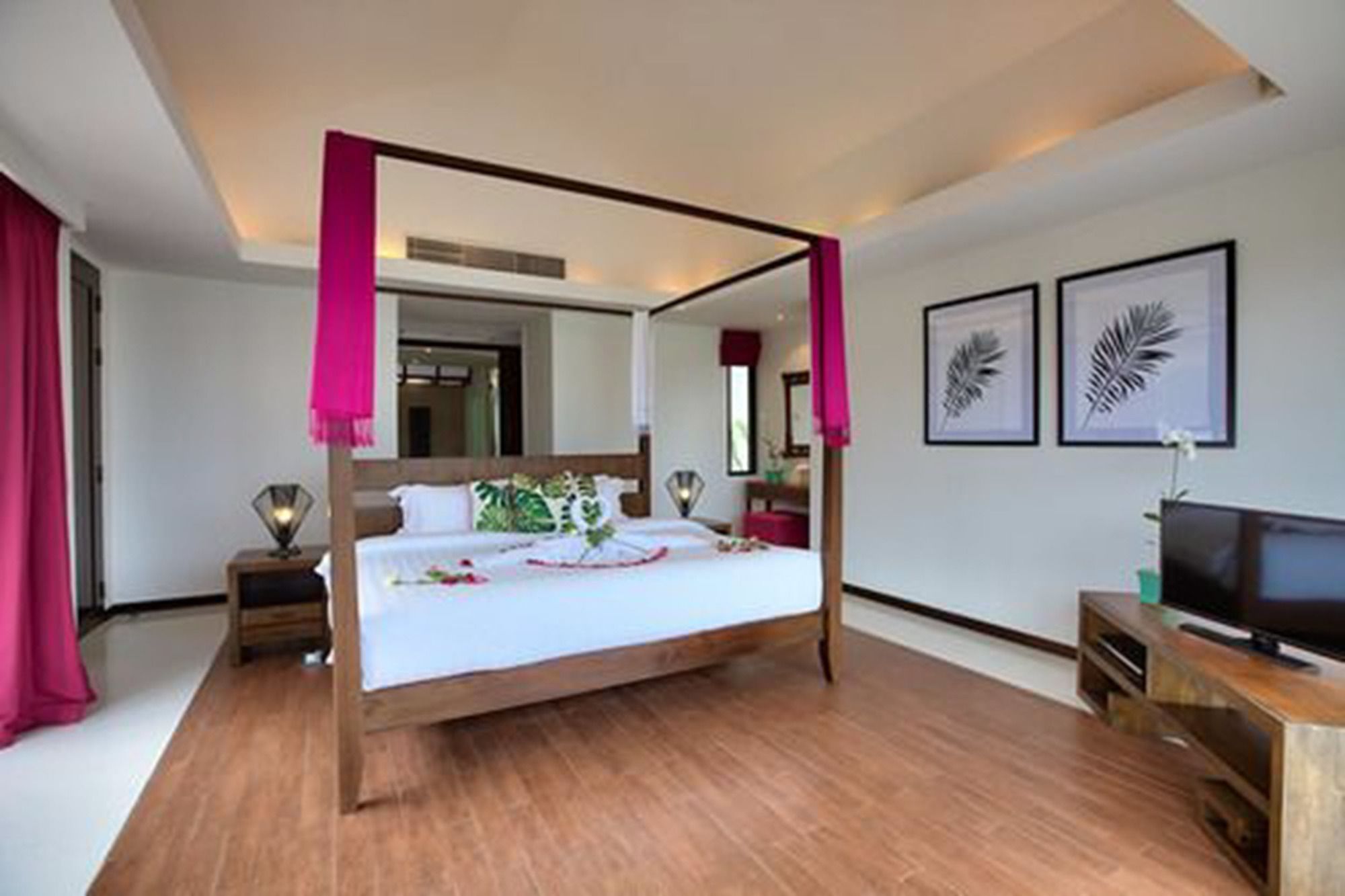 A hotel room with a four-poster bed, a television, and framed artwork on the wall.