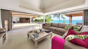 A spacious living room with a large window offering a view of the ocean, a sofa, a coffee table, and a dining area in the background. - Baan Benjamart (Koh Samui)