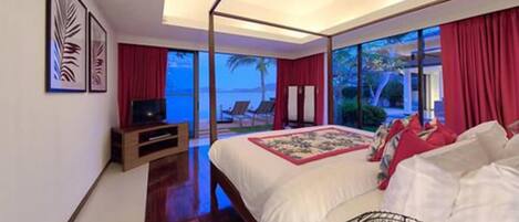 A bedroom with a large bed, a TV, and a view of the ocean.