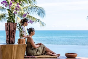 A woman sitting by the ocean with a wooden table and a plant. - Baan Benjamart (Koh Samui)