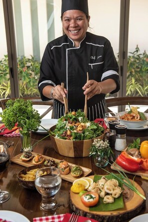 A chef in a black uniform with a chef's hat, standing behind a table with a variety of dishes, including pasta, seafood, and salads. - Baan Benjamart (Koh Samui)