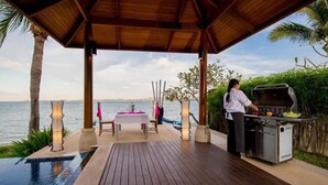 An outdoor dining area with a grill, a pool, and a view of the sea. - Baan Benjamart (Koh Samui)