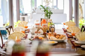 A breakfast table set with various food items, condiments, and a vase of flowers. - Baan Benjamart (Koh Samui)
