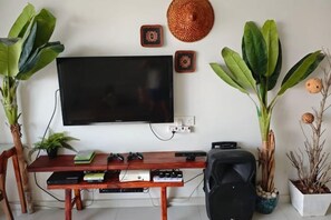 Een woonkamer met een flatscreen televisie aan de muur, een houten salontafel met elektronische apparaten en potplanten.