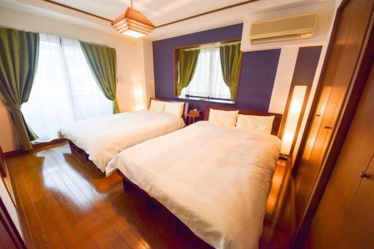 A hotel room with two beds, a window with curtains, an air conditioning unit, and a wooden floor.