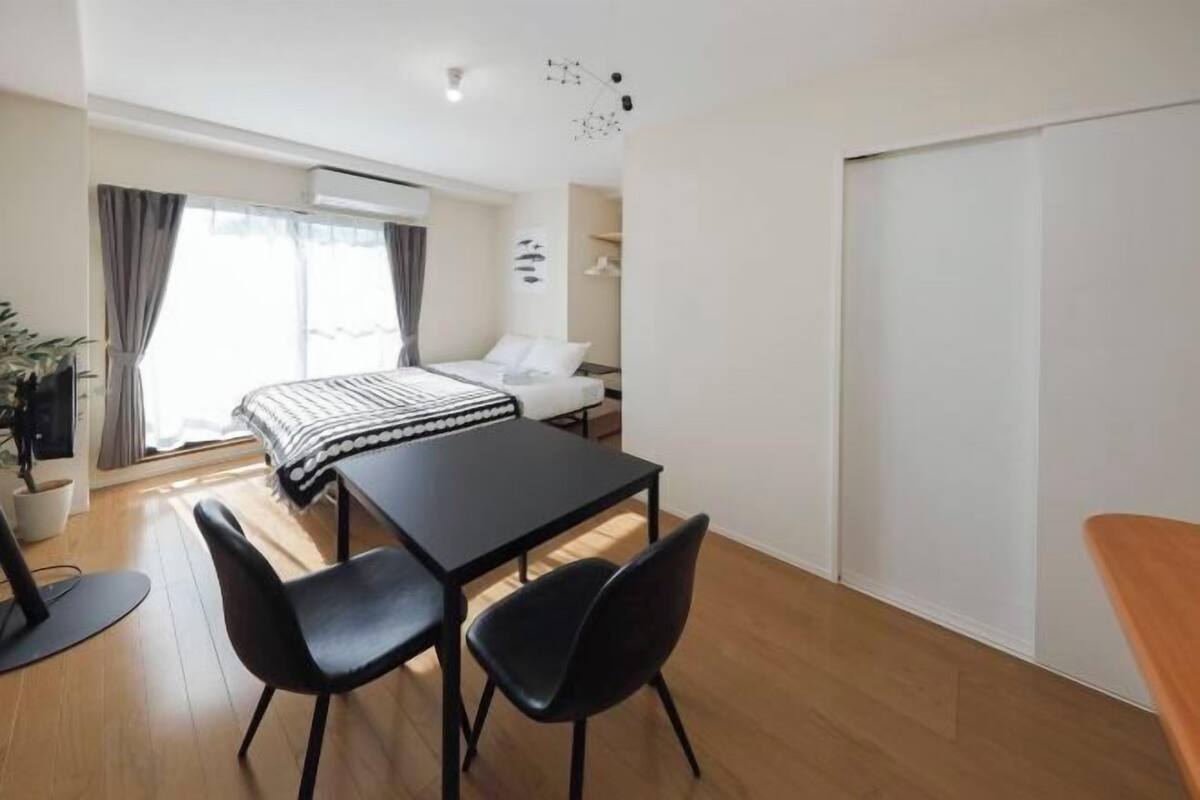 A modern, well-lit room with a bed, a dining table with chairs, a small desk, and a potted plant.