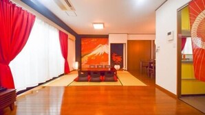 A hotel room with a tatami mat floor, a futon bed, a red curtain, a painting, and a traditional Japanese fan. - Ryokan -Ryo- by Tranova (Tokyo)