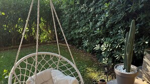 Una silla colgante con cojín en un jardín con un cactus y plantas en macetas.