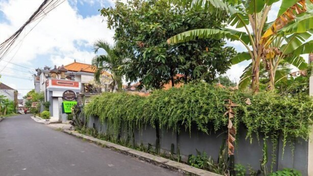 A narrow street lined with lush greenery and a building with a signboard. - Urbanview Asung 2 Guesthouse near Canggu (Bali)