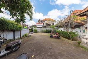 A courtyard with a motorbike, a scooter, and a red motorcycle parked. - Urbanview Asung 2 Guesthouse near Canggu (Bali)