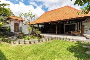 A traditional building with a tiled roof, a covered outdoor seating area, and a well-maintained garden. - Urbanview Asung 2 Guesthouse near Canggu (Bali)