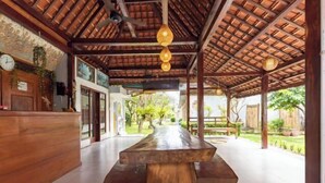 A covered outdoor dining area with a wooden table and benches, a clock, and hanging light fixtures. - Urbanview Asung 2 Guesthouse near Canggu (Bali)