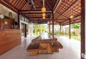 A covered outdoor dining area with a wooden table and benches, a clock, and hanging light fixtures. - Urbanview Asung 2 Guesthouse near Canggu (Bali)