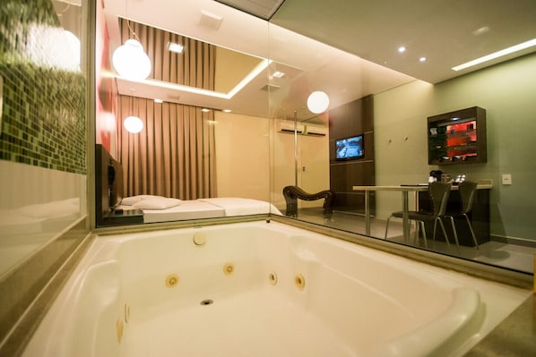 A modern bathroom with a large bathtub, a glass shower enclosure, and a seating area with a table and chairs. - Motel Vitara (Taboão da Serra)