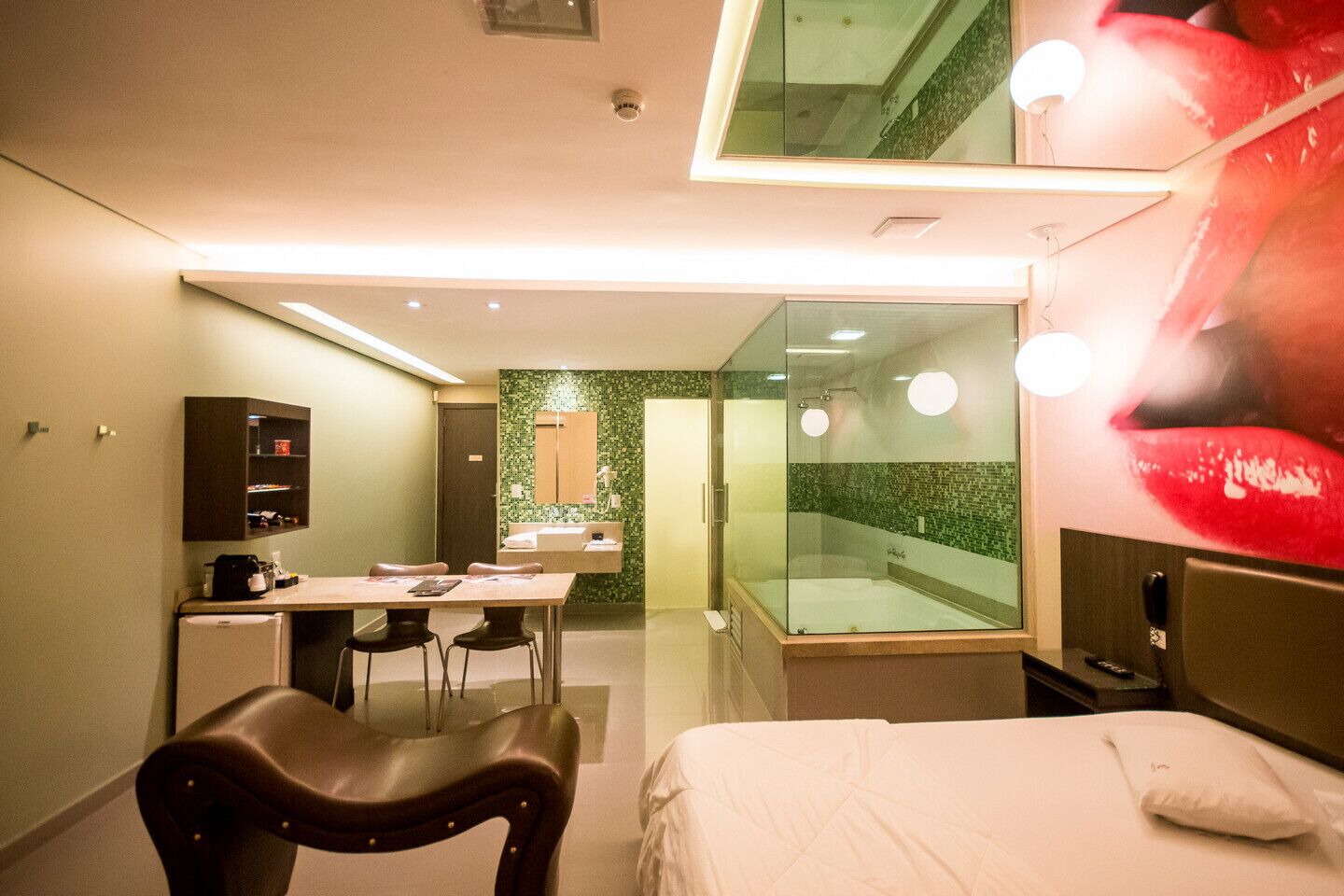 Habitación de hotel moderna con ducha de vidrio, zona de comedor con mesa y sillas, y cama con almohada grande.