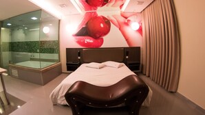 A modern hotel room with a glass-enclosed shower, a large bed with a headboard, and a unique ceiling design featuring red apples. - Motel Vitara (Taboão da Serra)