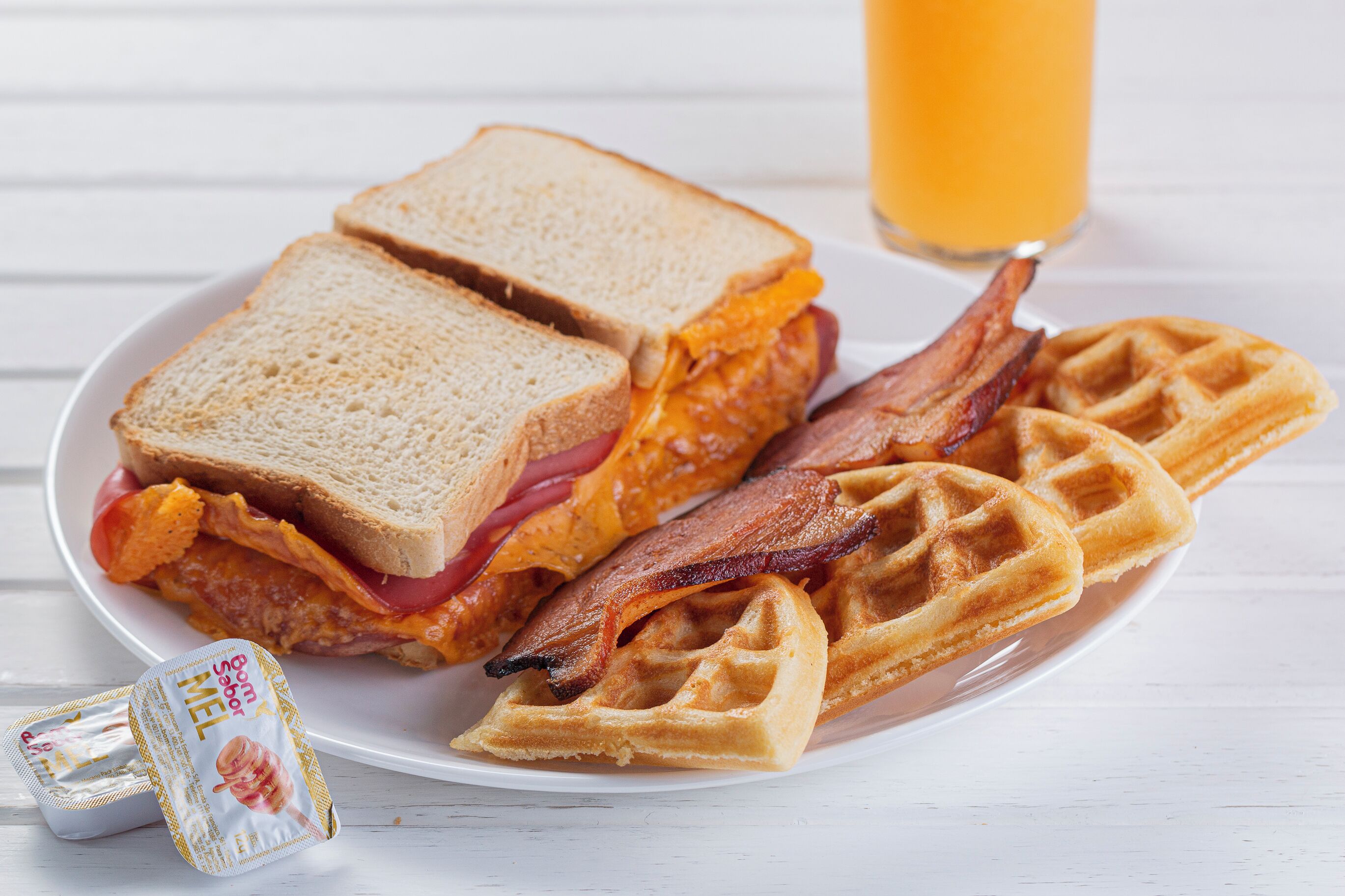 Une assiette avec un sandwich, du bacon et des gaufres.