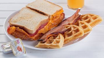 Une assiette avec un sandwich, du bacon et des gaufres.