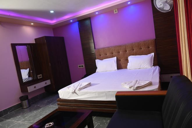 Una habitación de hotel con cama, mesita de noche, espejo y ventilador de pared.