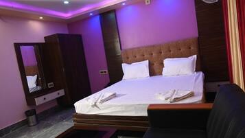 Una habitación de hotel con cama, mesita de noche, espejo y ventilador de pared.